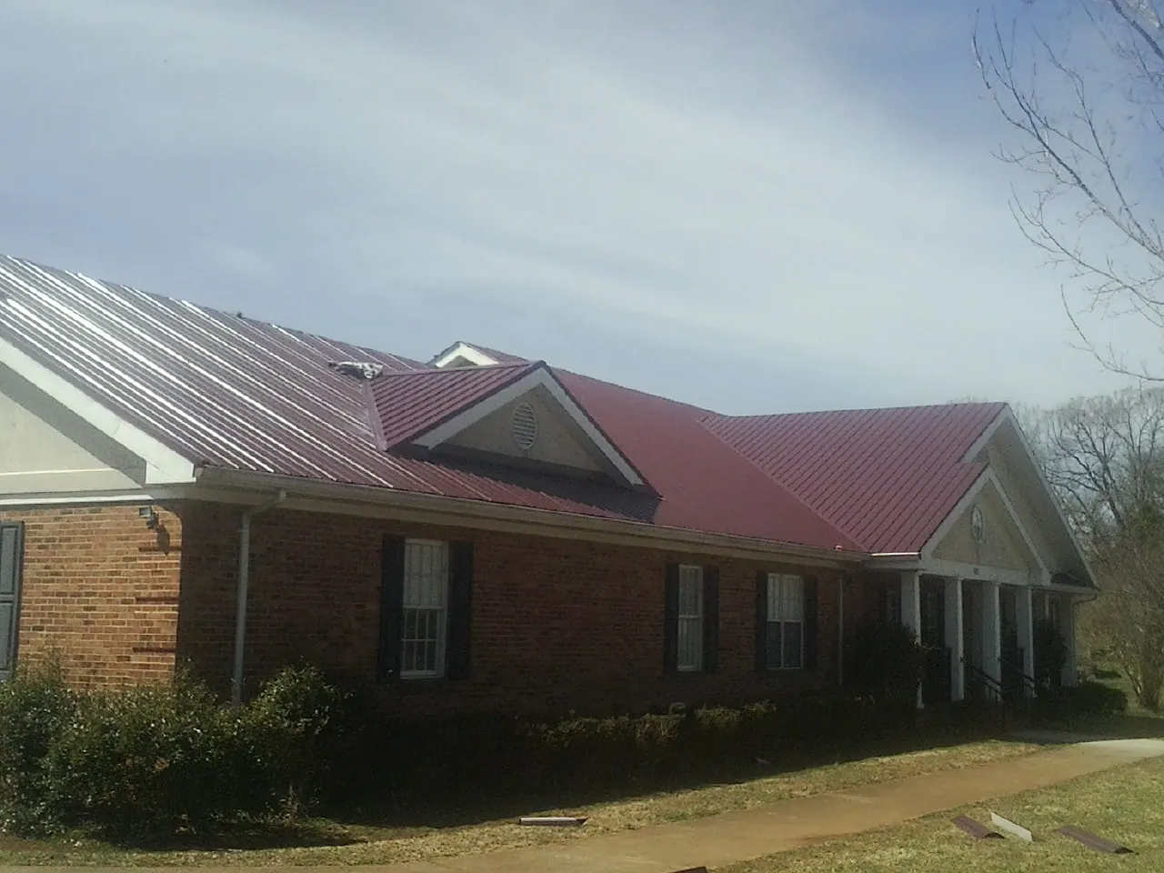 Red metal roof with gabled entries on a long brick building, from a Hail Damage Roof Repair job in Drayton
