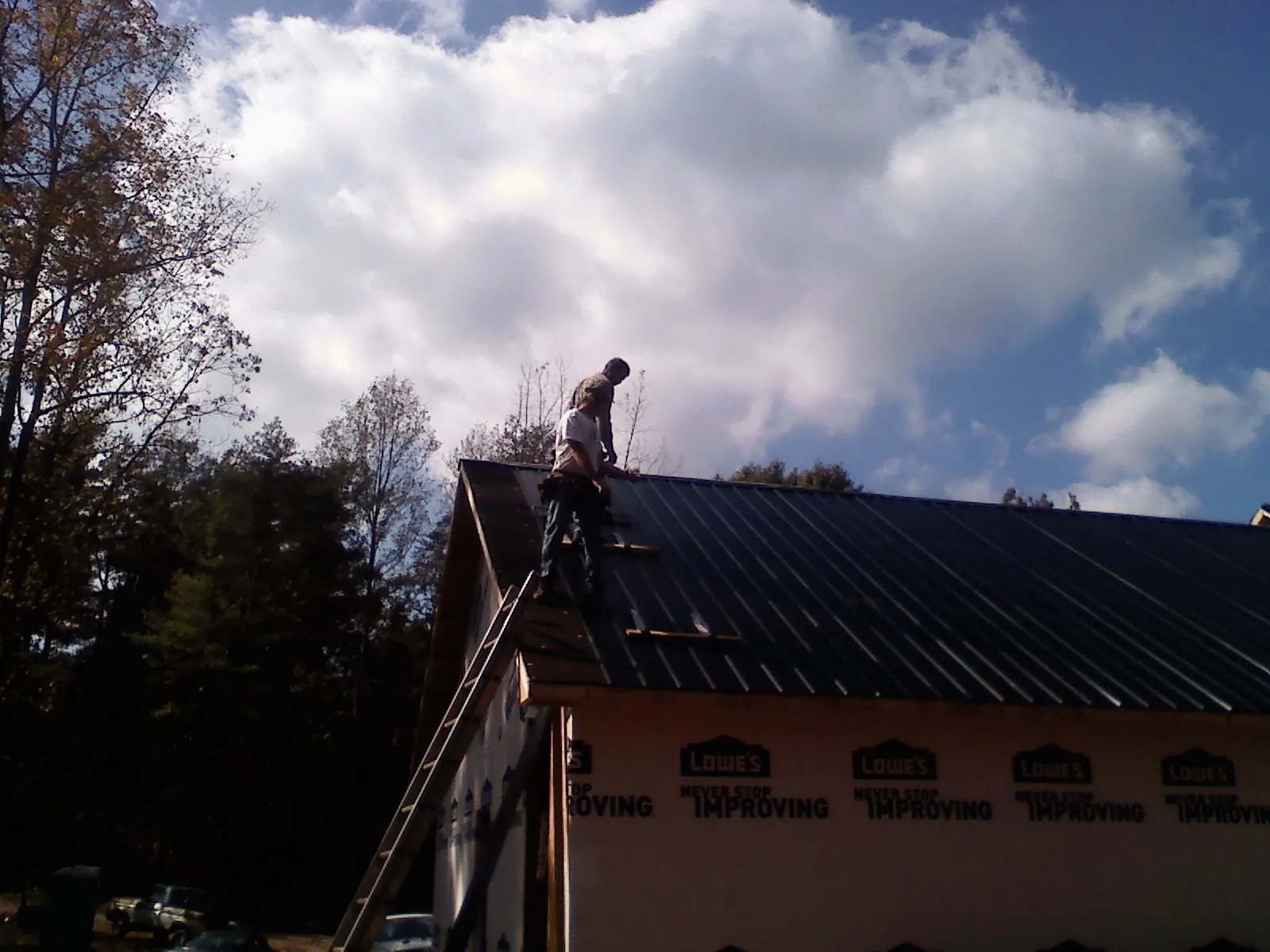 Roofer fastening dark metal panels high against a cloudy sky, from a Roof Inspection job in Drayton